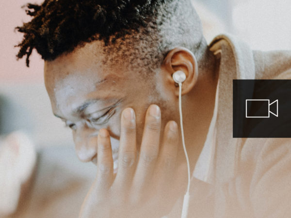 An African American man smiling as he is wearing ear buds and working on a computer