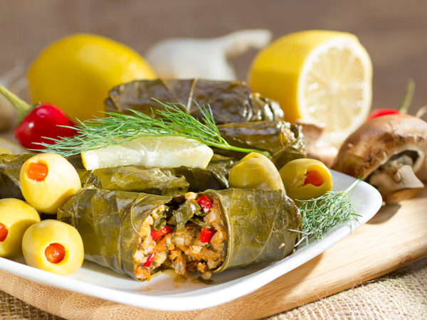 A plate of dolmas with green olives and lemon slices