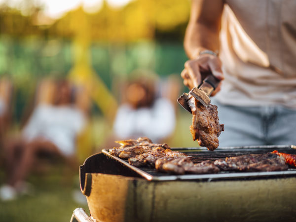Vlees op een BBQ op de voorgrond met mensen die in de verte socialiseren