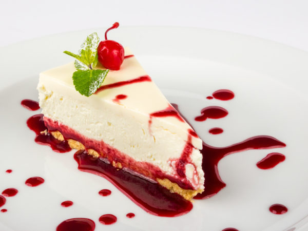A slice of cheesecake on a plate with cherry sauce over it