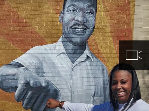 En ung svart kvinna som ger ett knytnävsslag mot en väggmålning av Martin Luther King Jr.