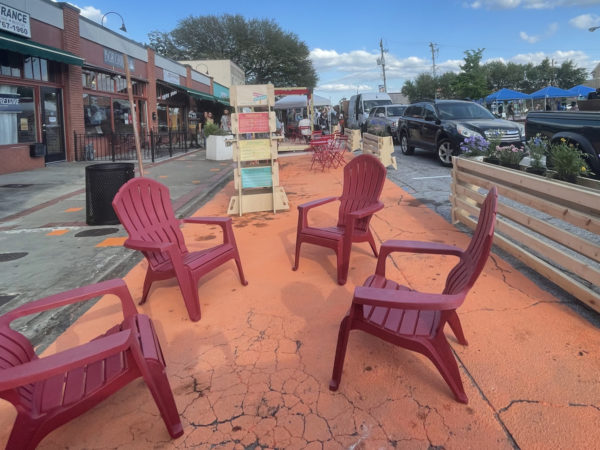 कुर्सियां, एक कियोस्क, और फूलों के साथ प्लांटर बॉक्स एक शहरी सड़क के किनारे स्थापित किए गए हैं