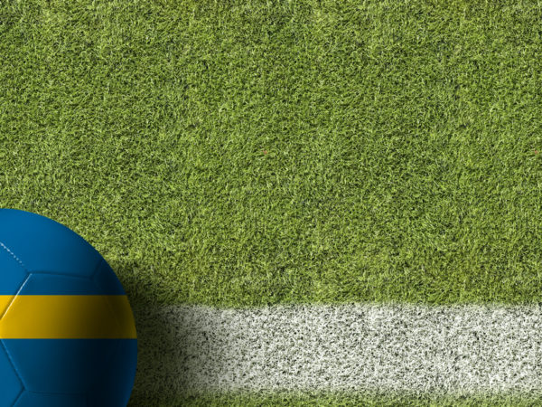 A soccer ball with a Swedish flag design lying on a turf field