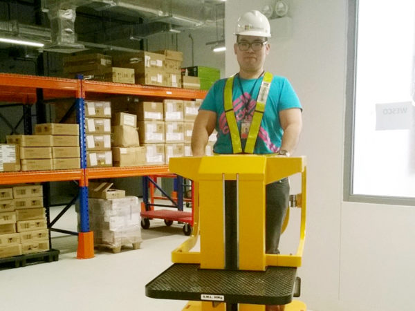 Desmond, wearing a hard hat, sitting on a lifting machine in a warehouse