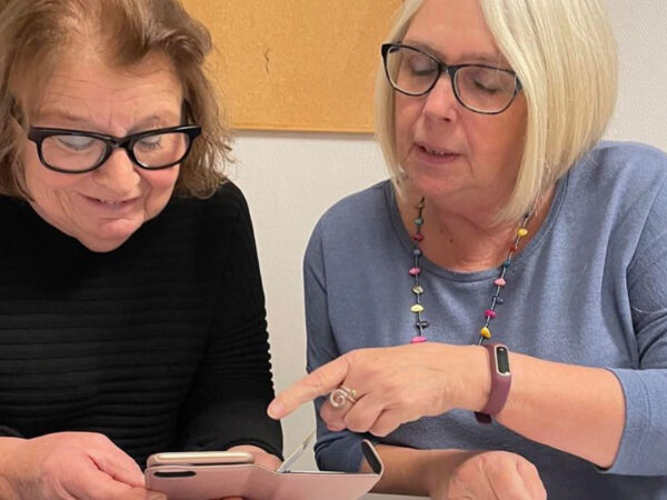 Seorang wanita menunjukkan kepada seorang wanita lanjut usia cara menggunakan ponsel