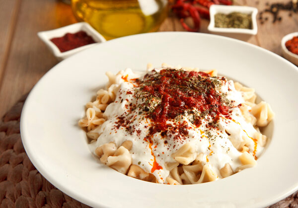 En tallerken med ravioli-lignende dumplings med hvid sauce og røde krydderier på toppen.