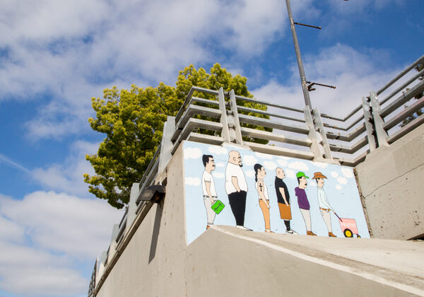 Ein Wandgemälde an einer Betonwand zeigt Männer, die in einer Reihe stehen