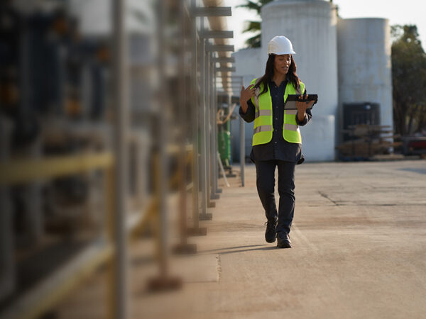 一位年轻的非裔美国妇女头戴建筑帽，身穿建筑背心，在建筑工地上行走