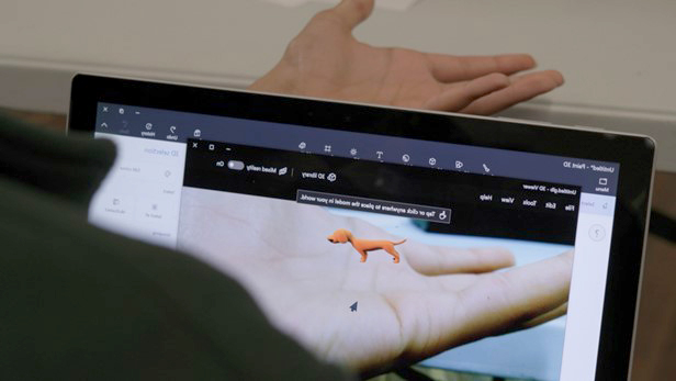 Tangan seorang anak muda di depan komputer dengan gambar digital seekor anjing di tangan