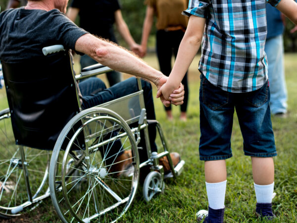 Een groep mensen houdt elkaars hand vast, één in een rolstoel