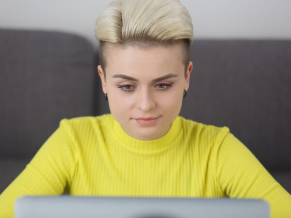 Schöne junge ukrainische Frau mit kurzen Haaren arbeitet am Computer. Porträt von stilvollen Tom Junge Person mit einem Laptop