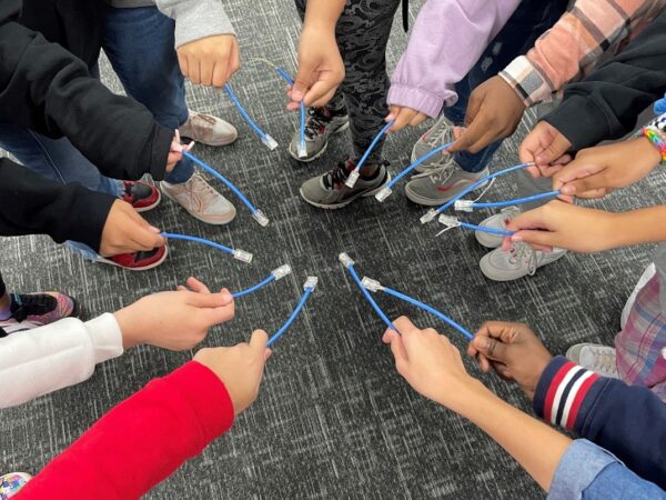 A number of young girls' hands all holding cables together in a circle