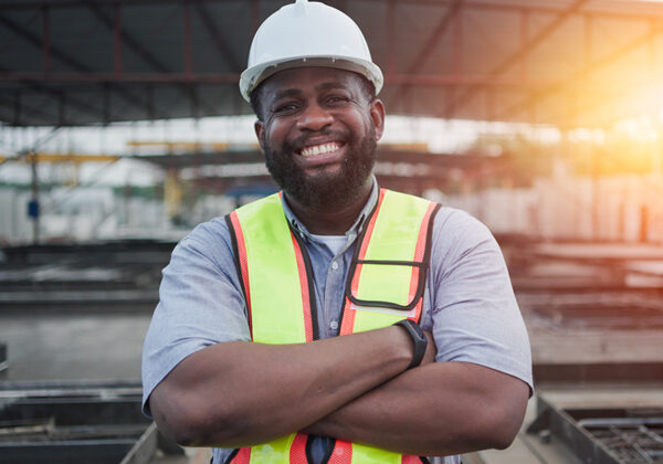 Um trabalhador da construção civil sorridente com um capacete e um colete amarelo brilhante