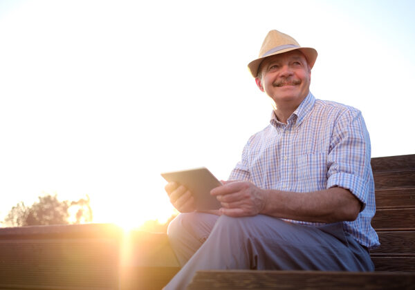 A senior man in Spain sitting on a park bench and using a tablet