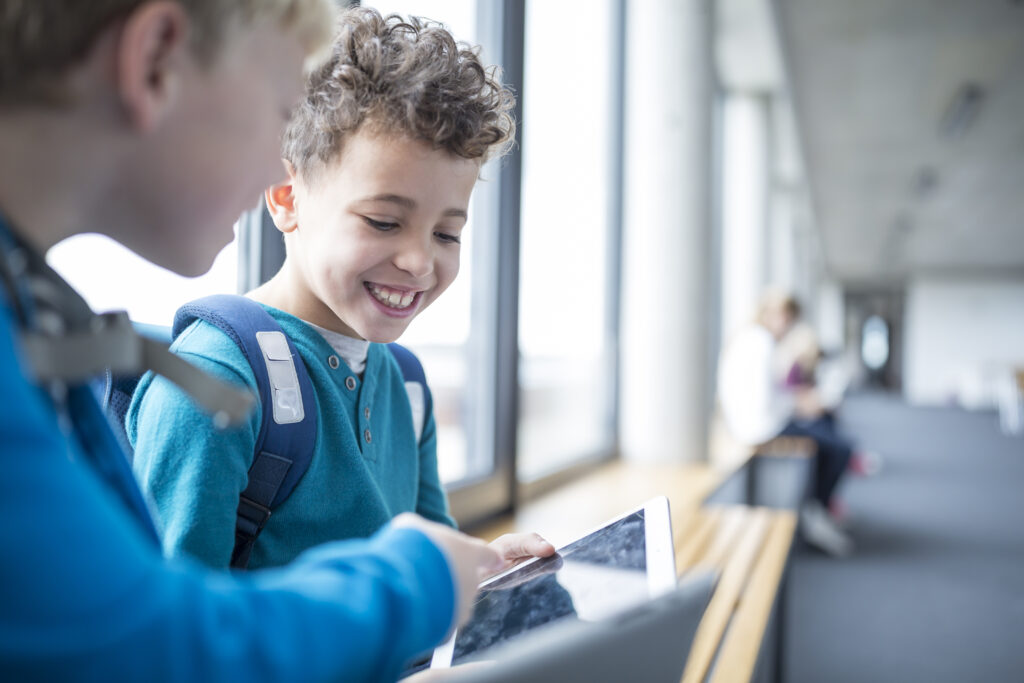 Smilende elever deler en tablet på skolegangen