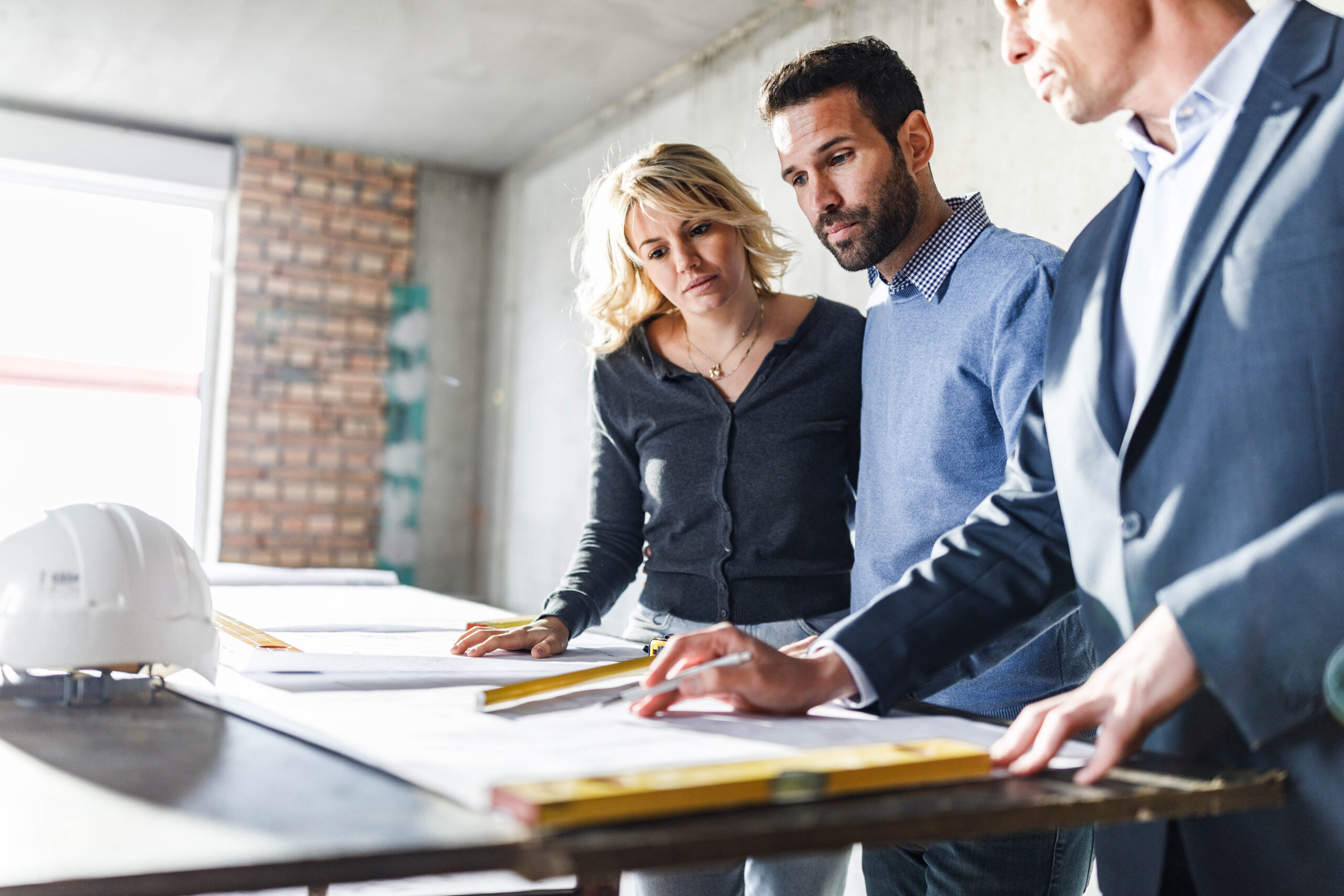 Three people analyzing blueprints at construction site.